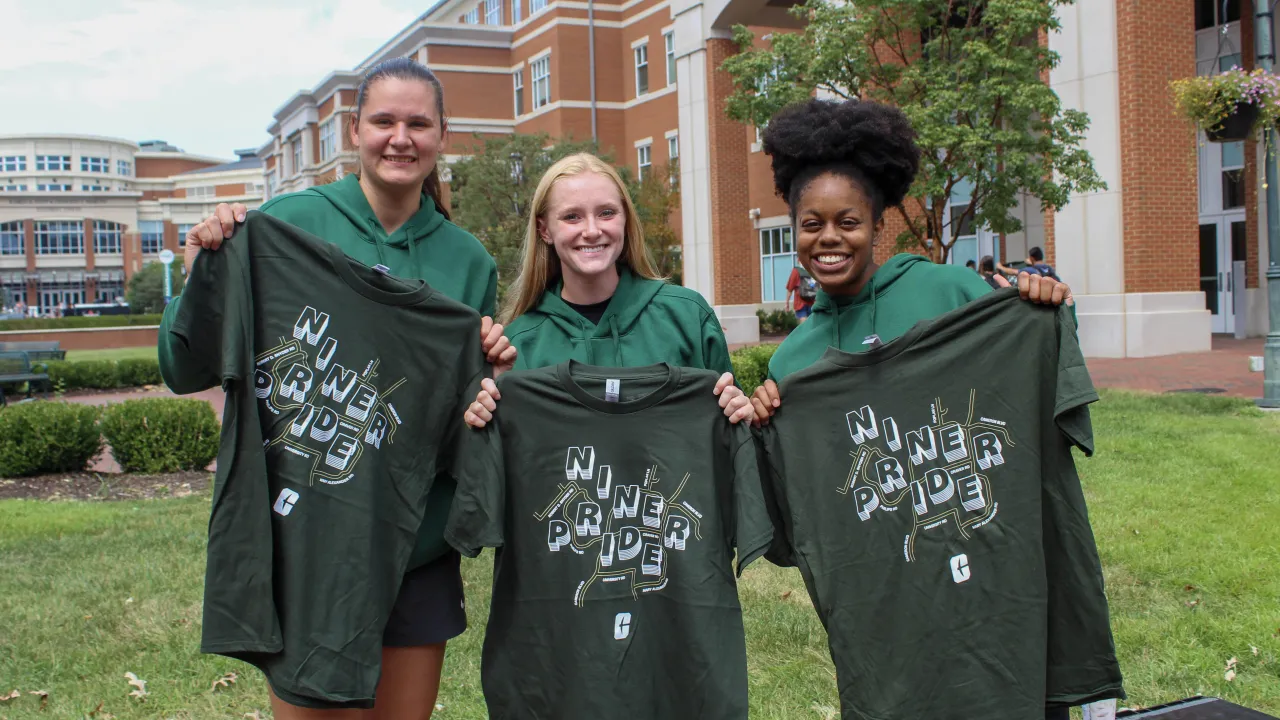 three students holding Niner Pride t-shirts 